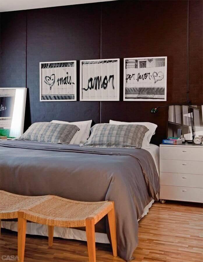 Quarto com parede de fundo preta, quadros com detalhes preto e branco, criado mudo branco, piso e bancos de madeira.