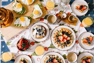 A table with plates of Waffles, Eggs, Orange Juice and other breakfast foods
