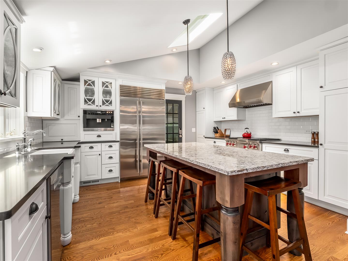 Newly renovated kitchen with traditional white beveled cabinetry and styled glass displays, dark contrasting countertops, stainless steel appliances and a natural wood island with a granite top.
