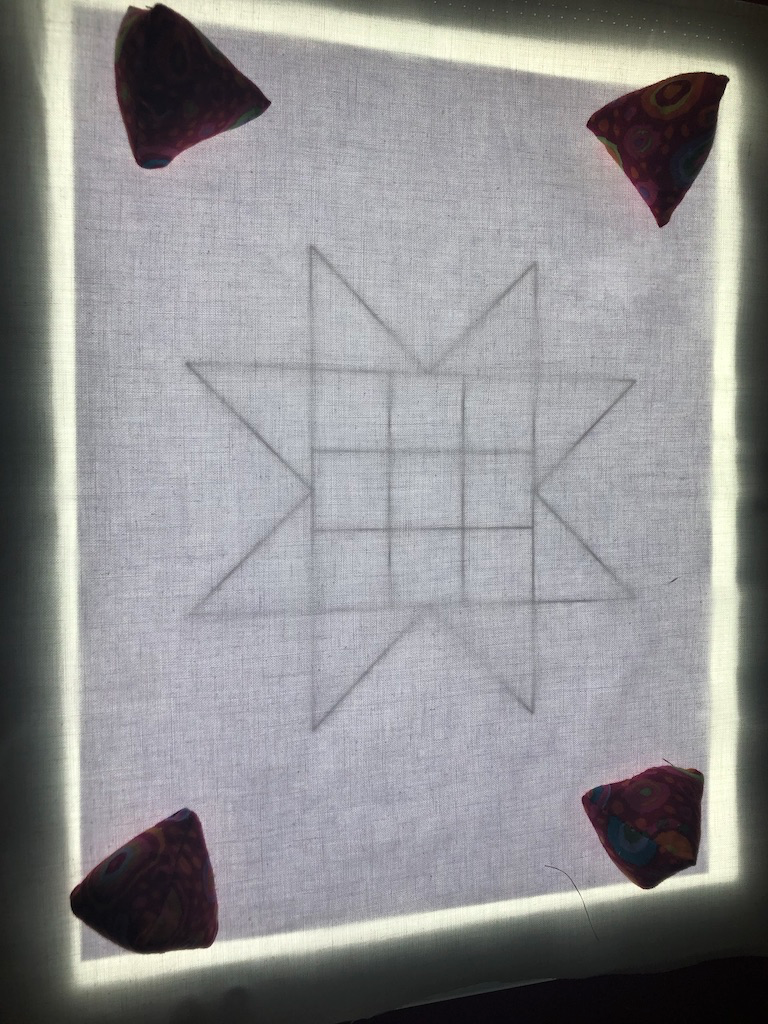 A quilt design backlit by a light pad 