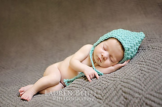 newborn lying on blanket wearing a teal baby bonnet