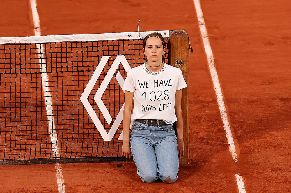 Kneeling woman protestor tied to tennis net wears t-shirt reading We Have 1028 Days Left