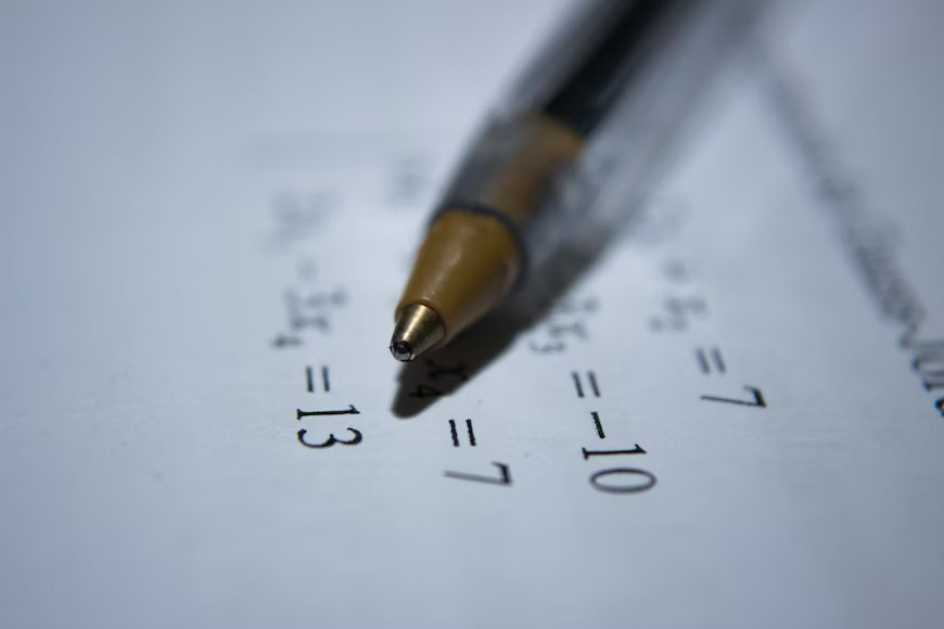A close-up photograph of a mathematical paper with handwritten equations and a pen.