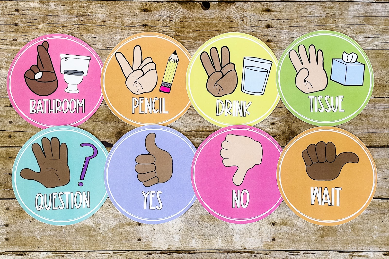 This image shows eight hand signal posters all on brightly colored backgrounds. The posters show common hand signals in the classroom, such as "Bathroom, Pencil, Drink, Tissue, Question, Yes,  No, & Wait". The posters are circular in shape and show multi-cultural skin tones. 