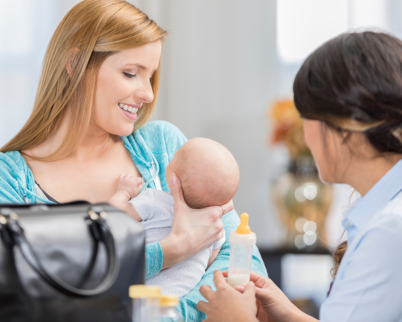 a mother smiling down at her new born with a caregiver holding a feeding bottle