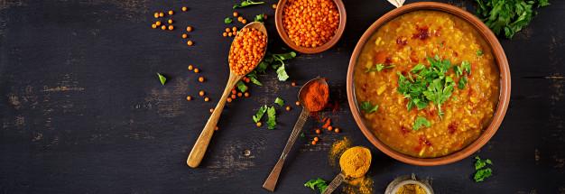 Indian dhal spicy curry in bowl, spices, herbs, rustic black wooden table. Free Photo
