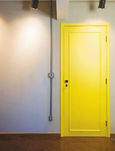 Ambiente com porta amarela, piso de madeira e parede branca.
