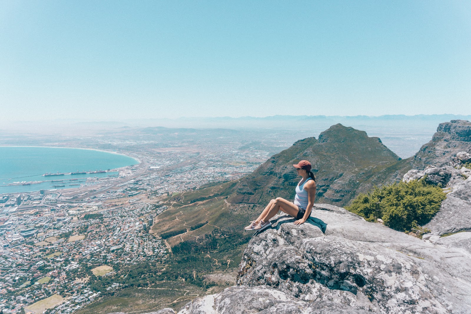 Best places for digital nomads: A girl with a baseball hat on sits on the edge of Table Mountain in Cape Town South Africa and enjoys the sweeping views.