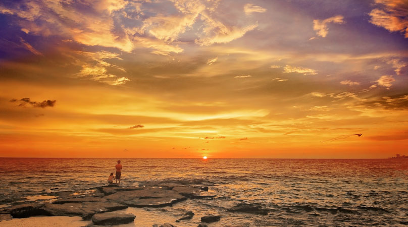 Two people are watching a vibrant sunset from Point of Rocks Beach in Sarasota, Florida.