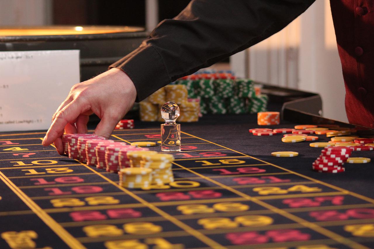 La mano de un croupier preparando varias filas de fichas de colores en un tablero de ruleta.