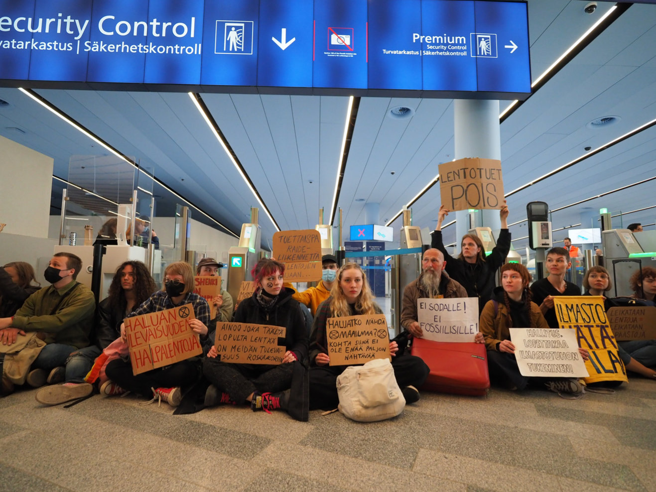 Young and older rebels holding placards sit on floor to block entrance to Security Control at airport