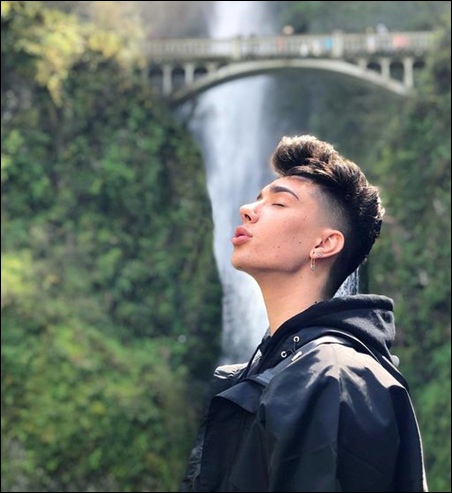 James Charles seen near a beautiful waterfall without any makeup, embracing his authentic self and absorbing the relaxing vibes of nature