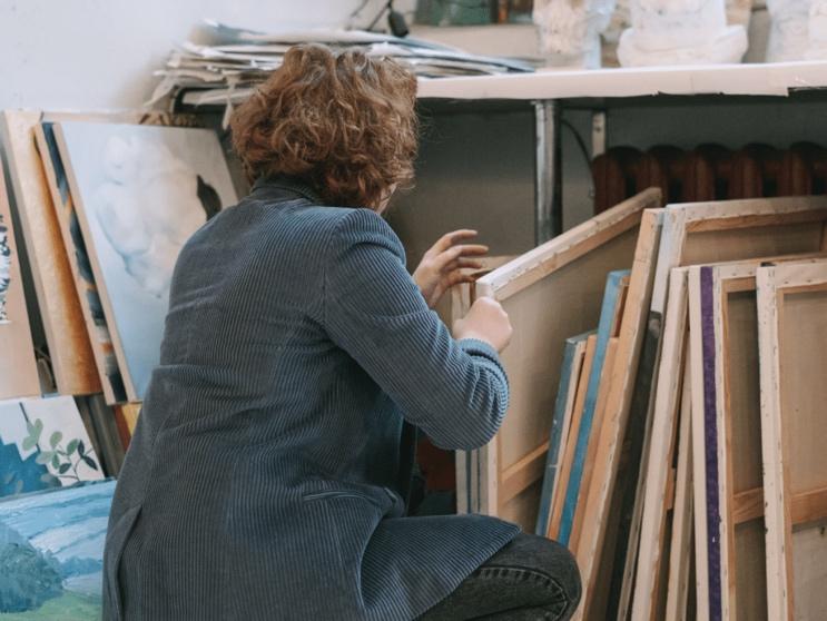 A person kneeling in front of a shelf with art

Description automatically generated