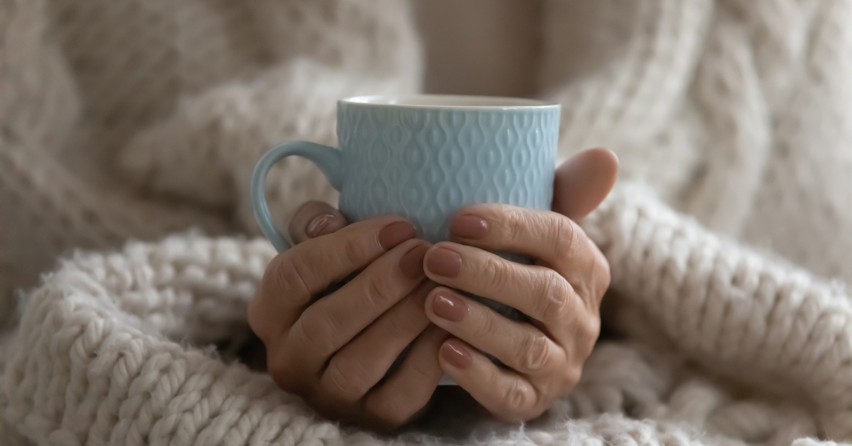 woman holding onto warm cup under blanket 