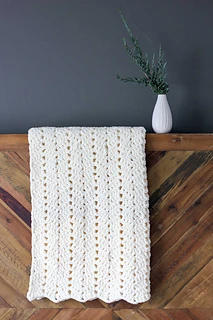 cream chunky crochet blanket folded and draped over a wooden backdrop