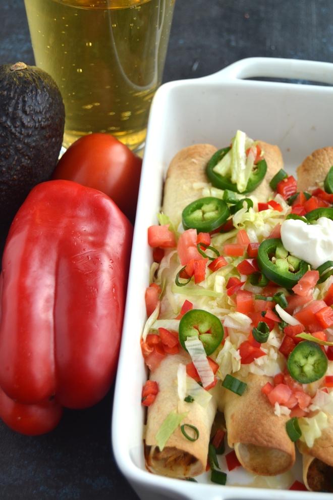 Baked Chicken Taquitos are filled with shredded chipotle chicken and melted cheese and are perfectly crispy. Topped with tomatoes, jalapeno, lettuce, sour cream, cheese and green onion for a delciious appetizer or meal! www.nutritionistreviews.com