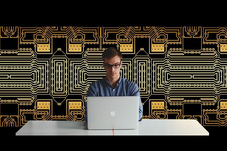 A man at a computer with circuit boards behind him.