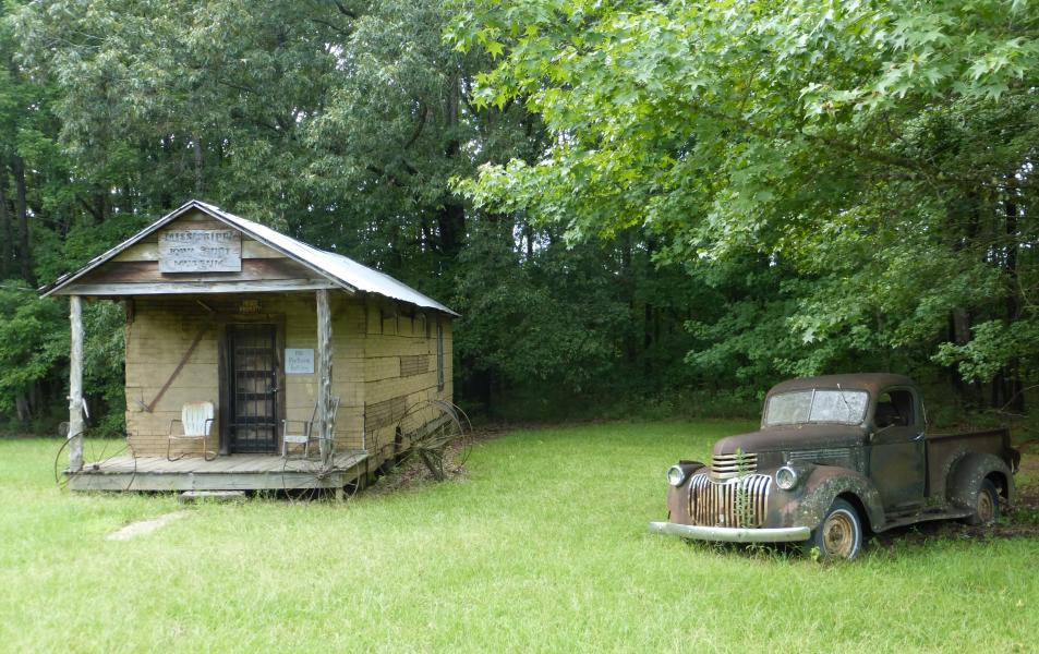 An old Mississippi house and rusted old pickup truck sit in a leafy grassy area. 
