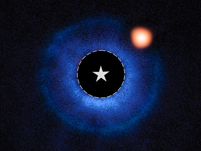Composite image of TWA 7 b, a Saturn-mass exoplanet, seen as an orange spot in a blue debris disk, captured by NASA’s James Webb Telescope’s MIRI and ESO’s VLT SPHERE. The star TWA 7’s light is blocked by a coronagraph, marked by a star symbol.