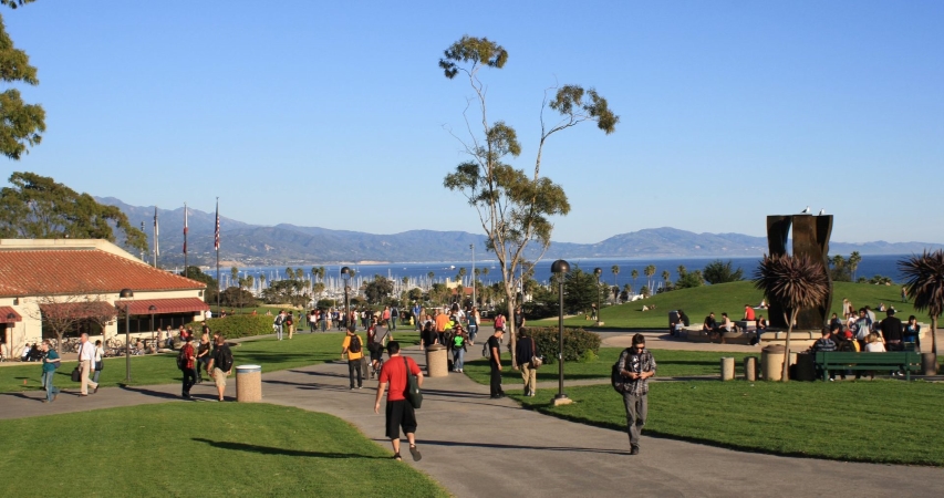 Students are walking through the gorgeous campus of Santa Barbara City College. The sky is a clear blue and you can see the mountains and ocean in the background.