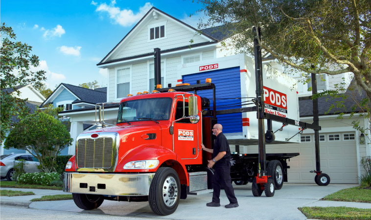 A PODS driver is using PODZILLA to lift a PODS container off of his truck and position it in a residential driveway.