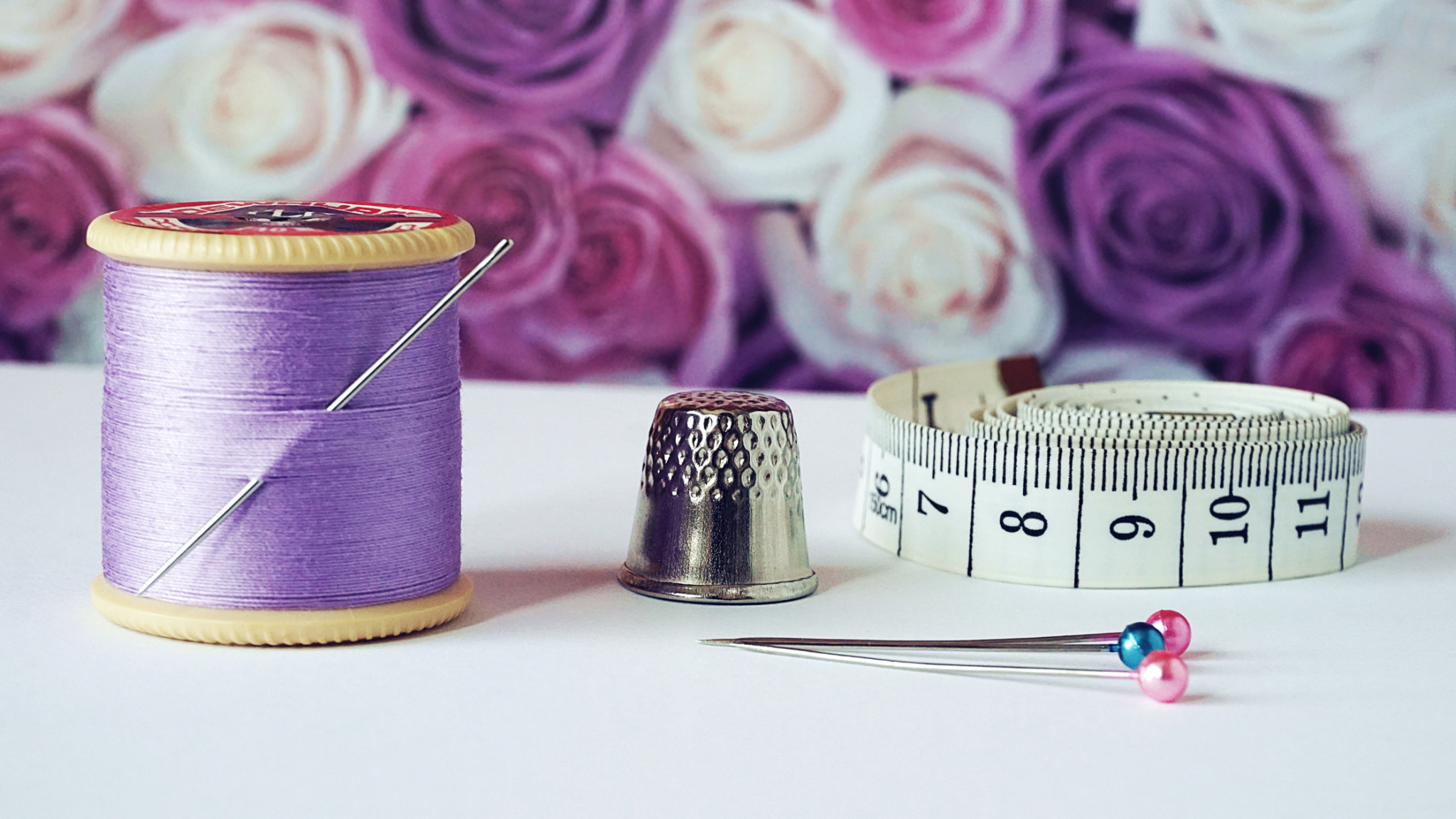 Lavender thread on spool with thimble, and tape measure on table