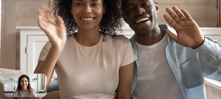 Image of couple in living room waving at a friend during video chat