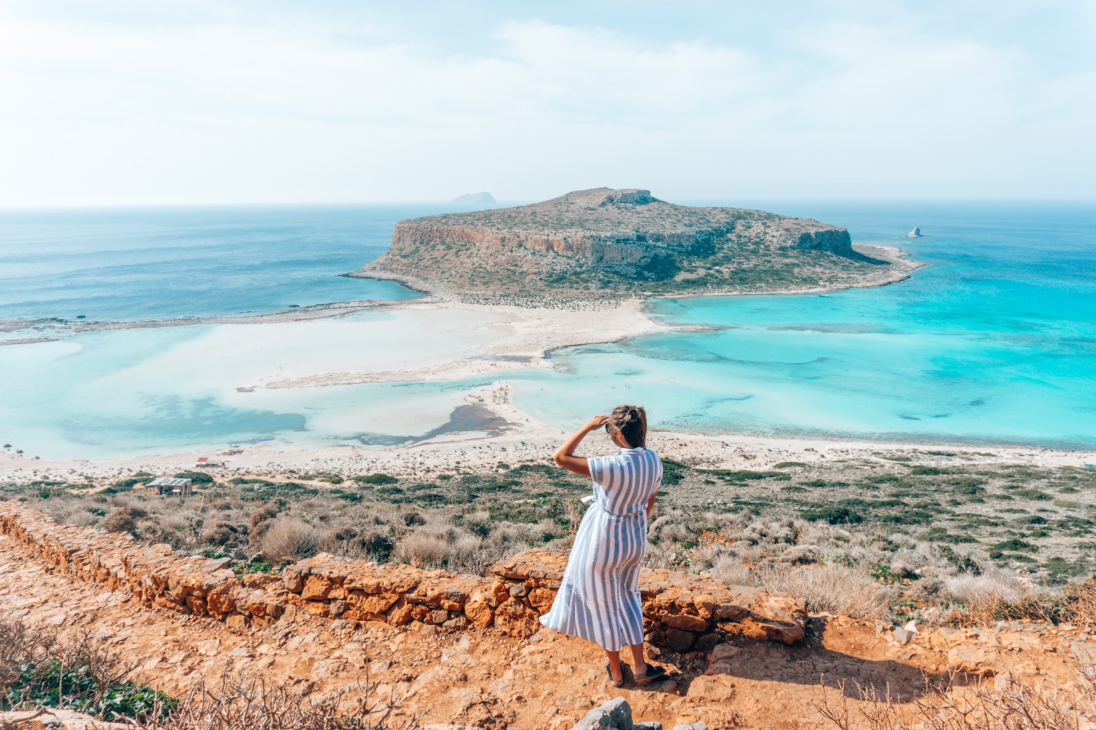 A girl in a dress looks out towards Balos Beach on Crete Island, Greece. 