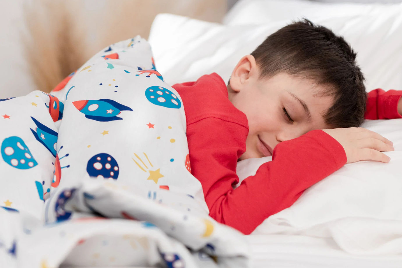 A child sleeping under a colorful Hush Kids Weighted Blanket with spaceship prints.