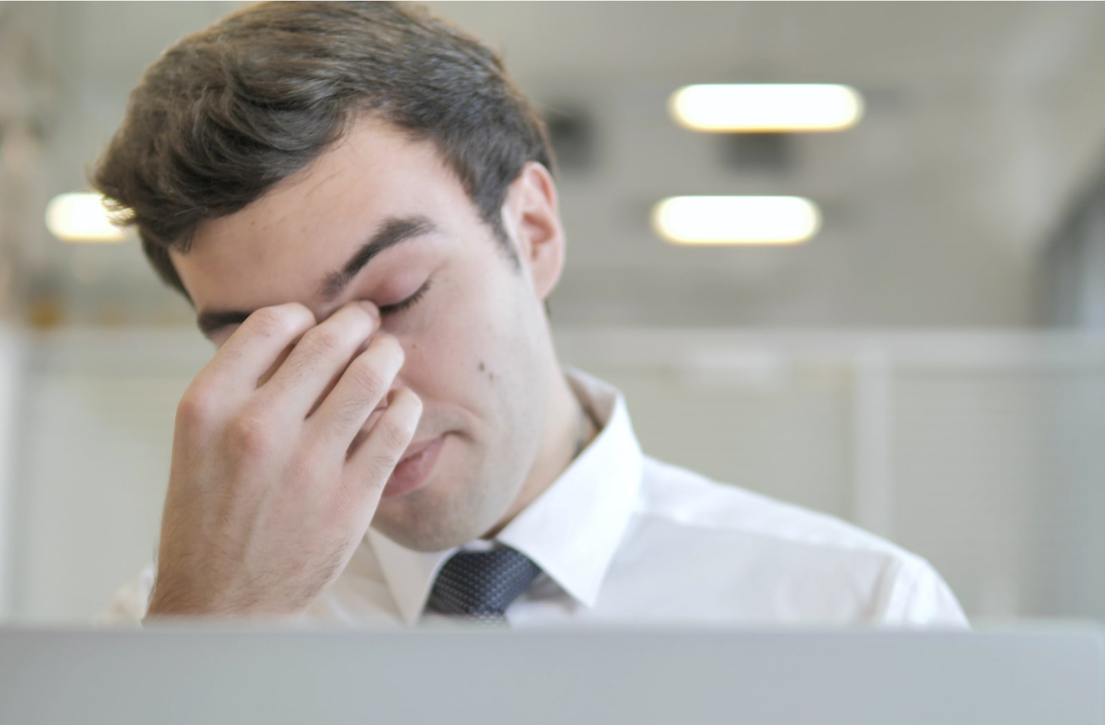 A young man at his desk with his eyes close and hand over his eyes due to digital eye strain