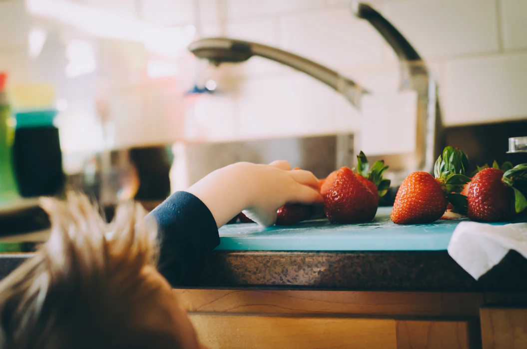 A child reaches for strawberries on a blue cutting board