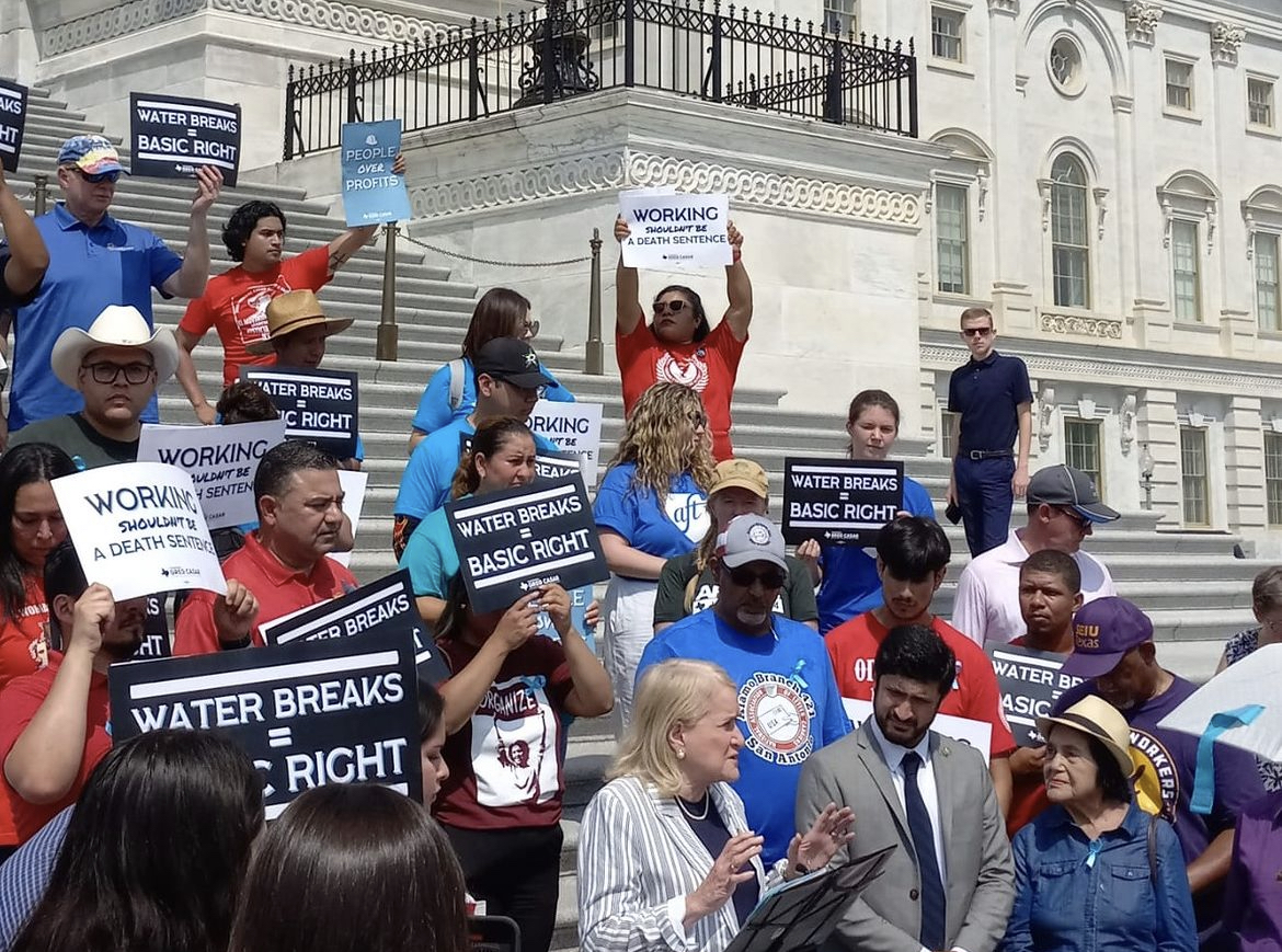 una toma desde un ángulo lateral de un grupo de personas con pancartas en el Capitolio de Texas protestando contra la política del Gobernador Greg Abbott que prohibía las pausas obligatorias para beber agua 