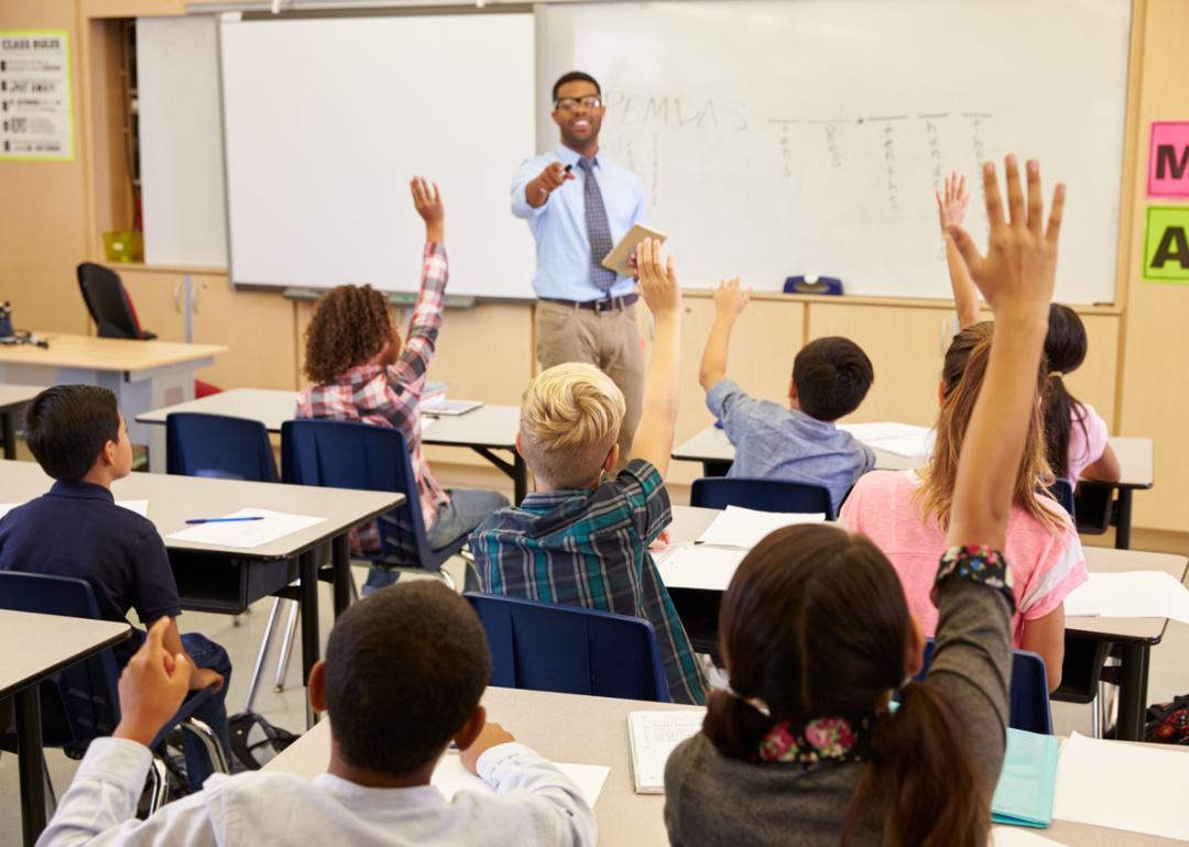 Kids raising hands in classroom.