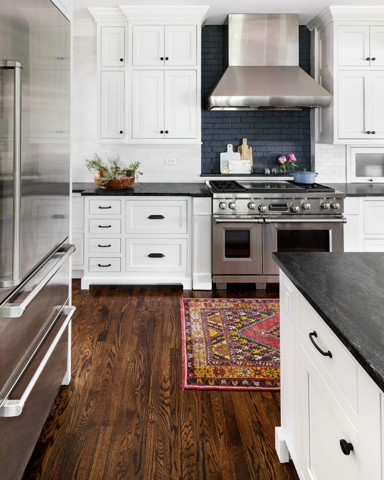 black and white farmhouse kitchen with white cabinets and black countertops. cabinets are white shaker style with black knobs and pulls. also features a dark wood floor, black brick backsplash and stainless steel appliances