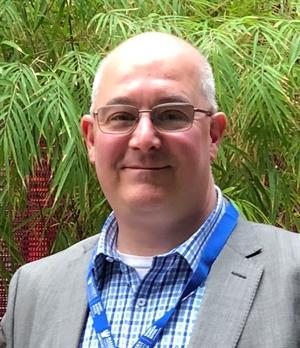 A person wearing glasses and smiling at the camera Description automatically generated