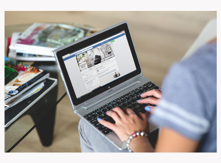 A person typing on an open laptop showinf a Facebook window.