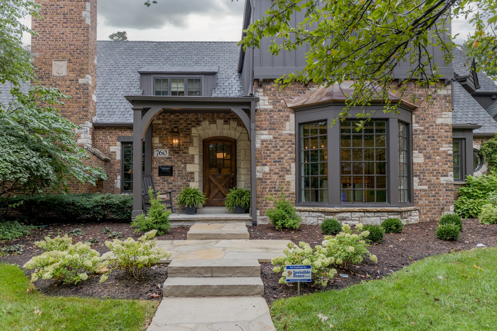 Exterior home entry with curb appeal featuring a brick and stone exterior, natural wood door and portico. 