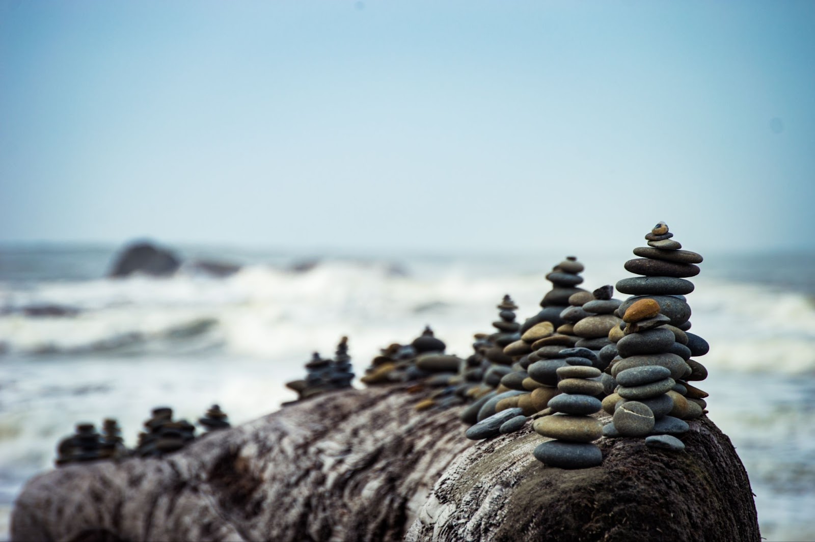 Multiple stacks of rocks on a large rock in along the ocean shore.