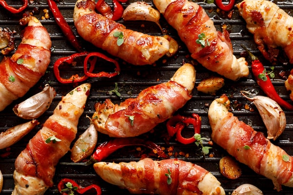 A grilled chicken tenderloin wrapped in bacon with wild chili, garlic, and herbs on a griller