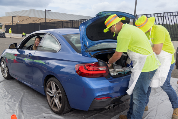 A person in yellow shirts and a blue car with the trunk openDescription automatically generated