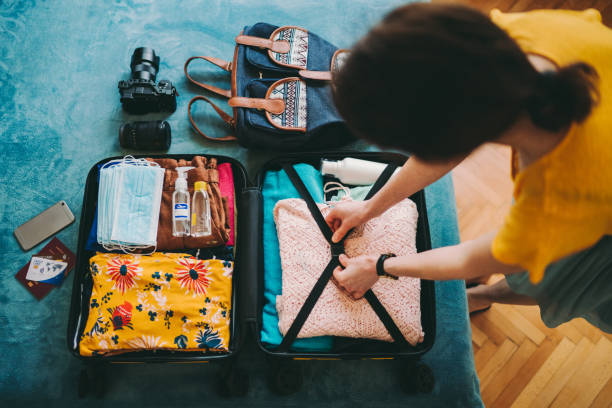 Woman packing suitcase for travel Woman packing suitcase for summer travel, including face masks and airplane travel-sized antibacterial hand gels packing bag stock pictures, royalty-free photos & images