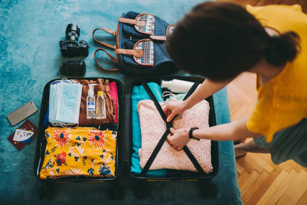 Woman packing suitcase for travel Woman packing suitcase for summer travel, including face masks and airplane travel-sized antibacterial hand gels  packing bag stock pictures, royalty-free photos & images