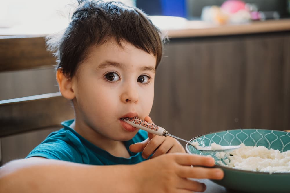 Child with spoon held backwards in their mouth eating breakfast