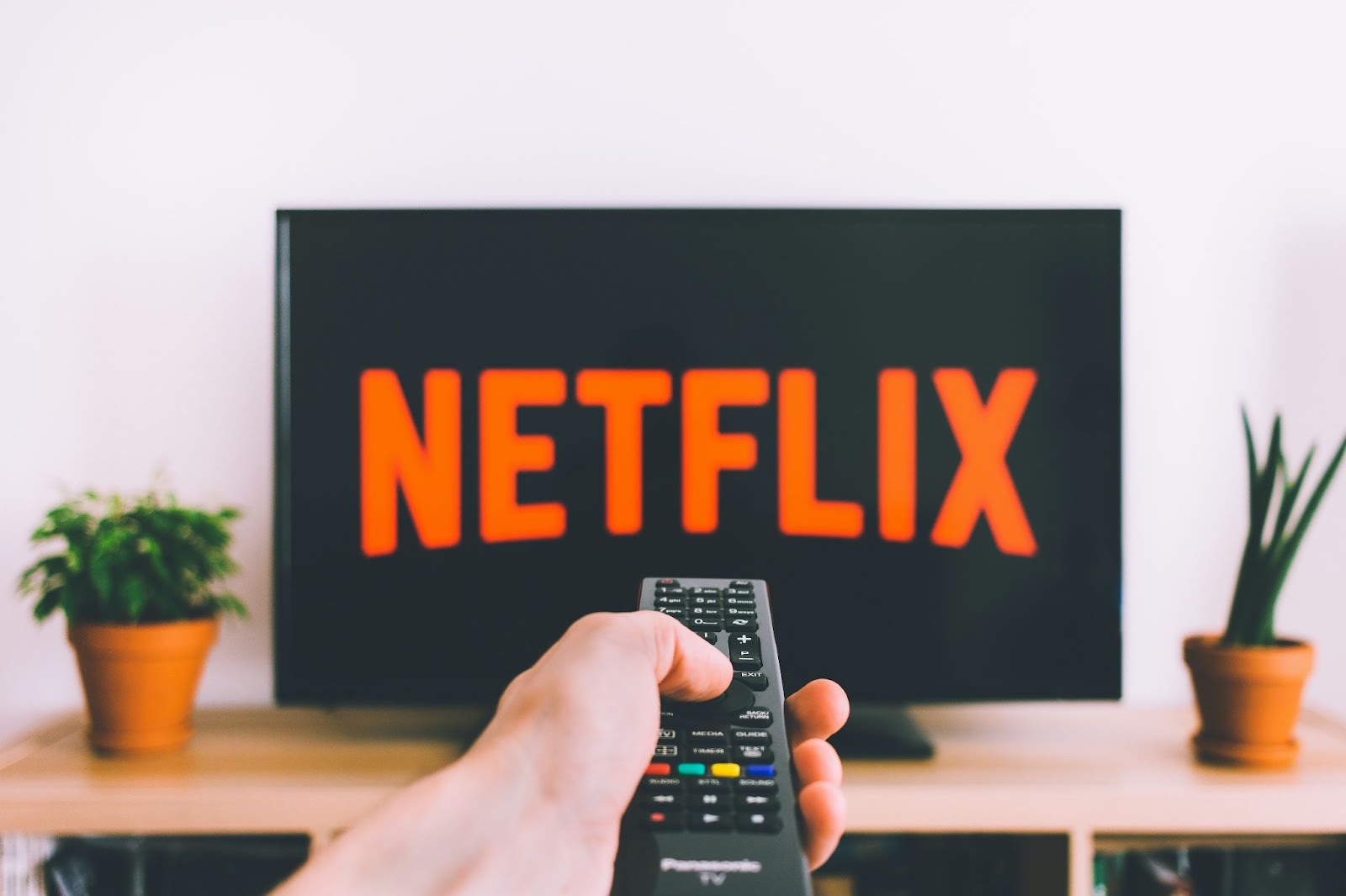 A hand holding a remote that's pointed at a TV screen showing the Netflix logo