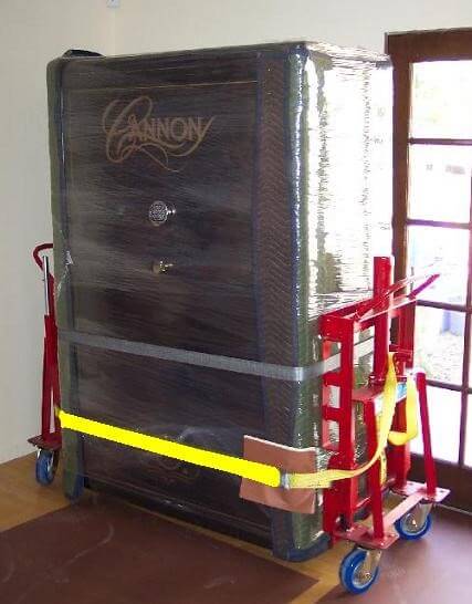 A picture of a black gun safe strapped in and sitting on top of a red moving dolly inside a home.