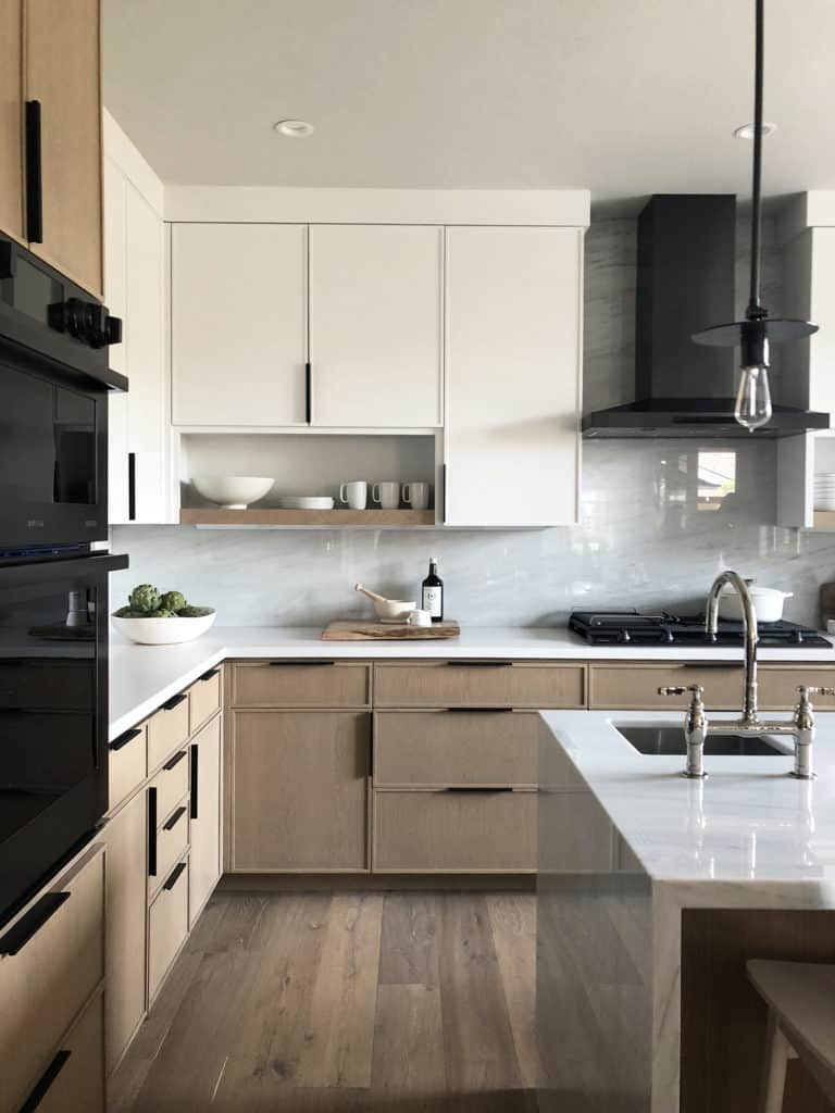 modern kitchen with white and brown cabinets, matte black modern cabinet hardware, glossy white backsplash and black appliances