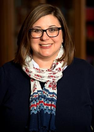 A person wearing glasses and smiling at the camera Description automatically generated