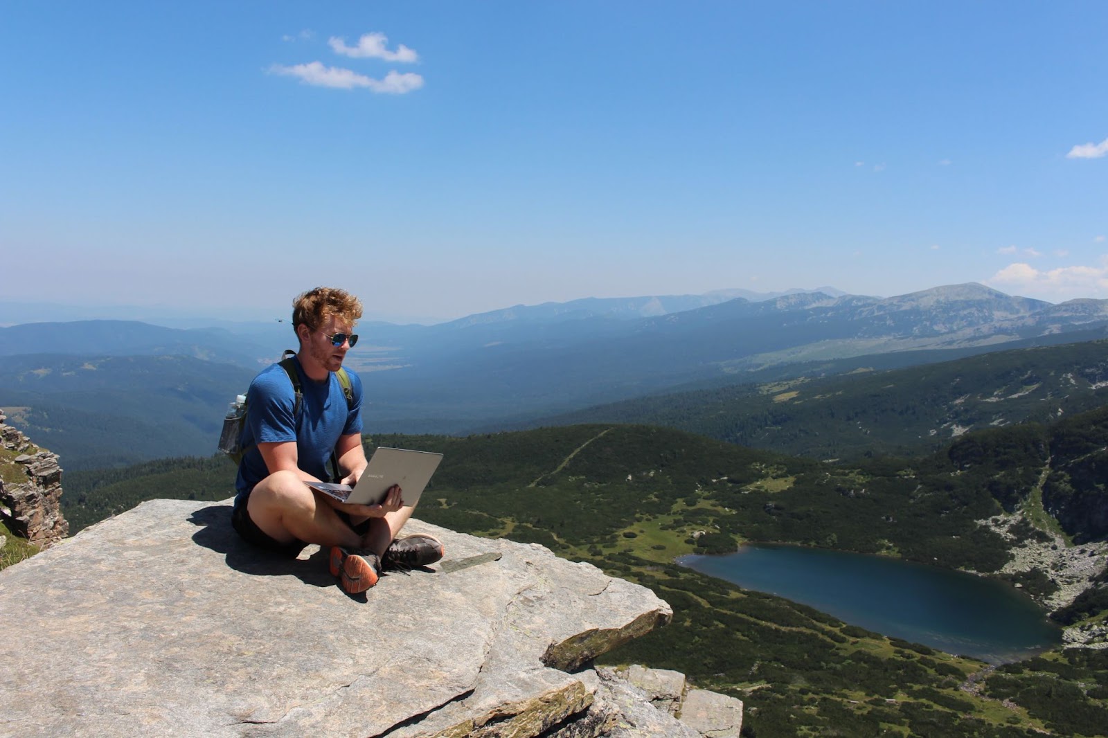 A man using his laptop at the top of a mountain