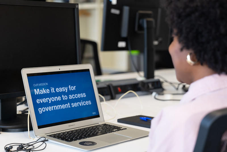 Image of a person looking at the screen of an open laptop. The focus is on the screen and it says "Our mission: Make it easy for everyone to access government services"