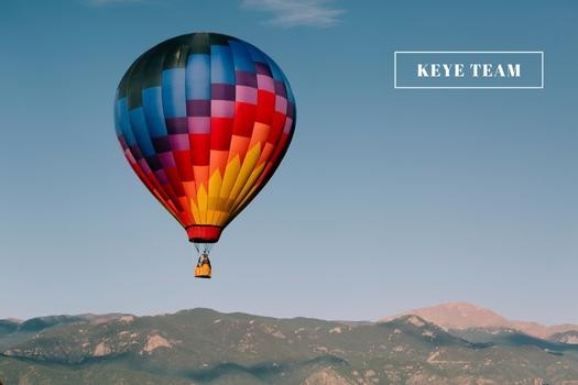 A vibrant hot air balloon is floating above the picturesque city of Park City, Utah, in the early morning light. The vivid colors contrast against the summer mountain background, creating a breathtaking view.